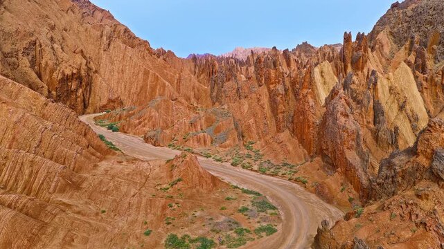 Aerial view of a winding dirt road through rugged red rock canyon ridges in the Red Mountain Stone Forest, Kuqa, Xinjiang, China