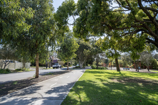 Paved bicycle and pedestrian path running through a leafy parkland reserve alongside a quiet residential street in Yarraville, inner west Melbourne, Victoria, Australia