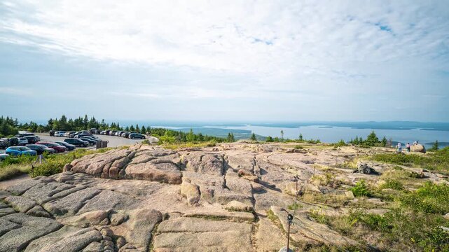 Acadia National Park, Maine timelapse showing tourists walking across the granite bedrock summit of Cadillac Mountain while cars fill the parking area overlooking Frenchman Bay.
