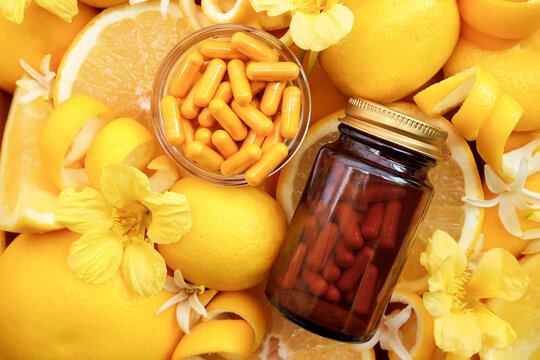 Yellow pills on bright citrus fruits background, bottle of vitamin C, natural medicine concept image, selective focus, shallow DOF