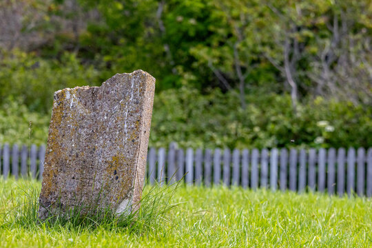 Gaspesie, Quebec, 15 July 2026 : A weathered concrete post stands in green grass with a blurred wooden fence and foliage in the background