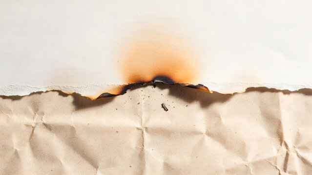 Burnt edge of a piece of paper with a scorched texture and charred border on a crumpled beige background