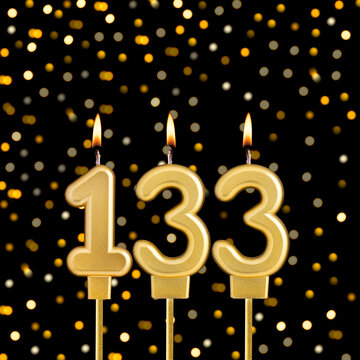 Number 133 birthday candle on a black background with blurred lights