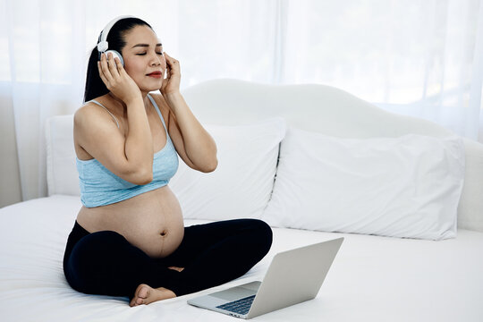 Pregnant woman wearing headphones and listening to music with laptop on bed at home, enjoying calm relaxation, maternity wellness and peaceful digital entertainment