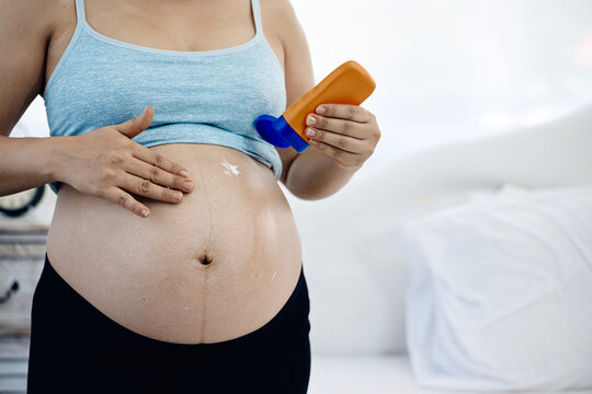 Pregnant woman applying lotion to belly for skincare, moisturizer, maternity pregnancy care and body hydration at home