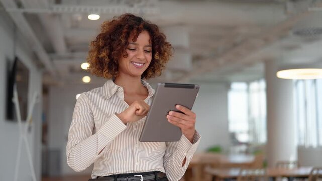 Hispanic business woman using digital tablet in modern coworking office, scrolling company report. Young latin professional checks financial data online, browsing fintech application at workplace