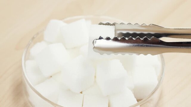 Metal Tongs Picking Up White Sugar Cube from Glass Bowl