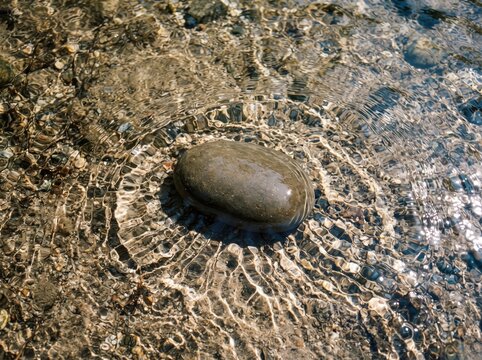 Smooth river stone resting on pebble seabed with rippling clear water overhead.