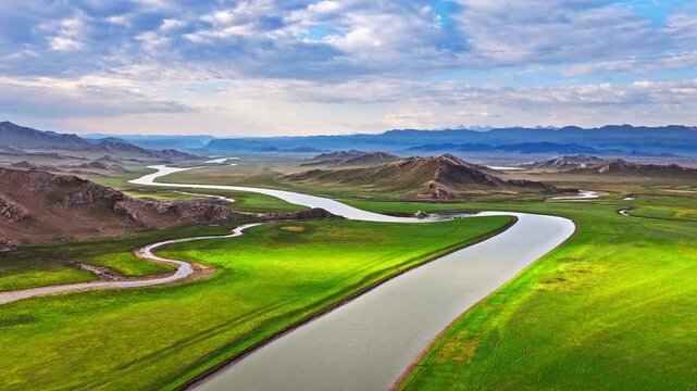 Aerial view of a meandering river flowing through lush green meadows in Bayinbuluke Grassland, Xinjiang, China