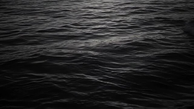 Dark sea surface gentle wave texture with subtle silver light, black water ripple patterns creating moody abstract ocean background for calm reflection and atmospheric coastal design