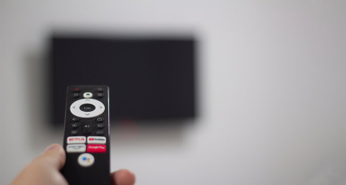 Tbilisi, Georgia - June 10, 2026: Photo close up with selective focus. Male hand holds black tv remote control with logos of Youtube, Prime video, Netflix, Google Play, Shivaki in hotel living room