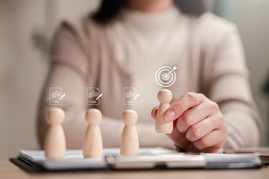 Human resources recruitment target and talent acquisition headhunting. Woman hand picking chosen wooden figure candidate with bullseye mark.