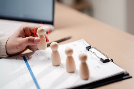 Human resources recruitment headhunting and talent acquisition. Woman hand picking chosen wooden figure candidate with target crosshair mark.