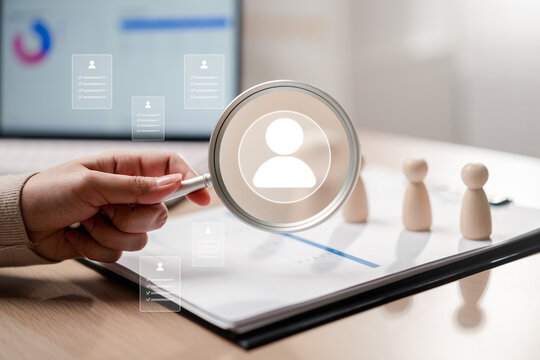 Human resources recruitment and candidate selection search. Woman hand holding magnifying glass over candidate profile resume and wooden figure.