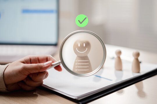 Human resources recruitment and candidate selection search. Woman hand holding magnifying glass over chosen wooden figure with check mark.