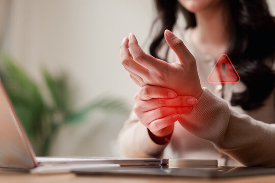 Office syndrome carpal tunnel health problem and wrist pain injury warning. Woman massaging hurting hand while working on laptop.