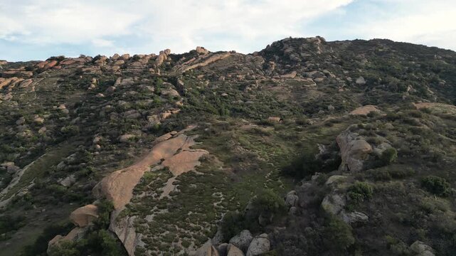 Aerial low approach towards rocky Santa Susana Mountains hillsides in the Santa Susana Knolls area of Simi Valley, California. Shot on an overcast afternoon, January 2024.