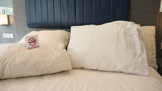 Clean modern hotel room with white bed linen, soft pillows, blue padded headboard and a visible non-smoking sign for guest accommodation