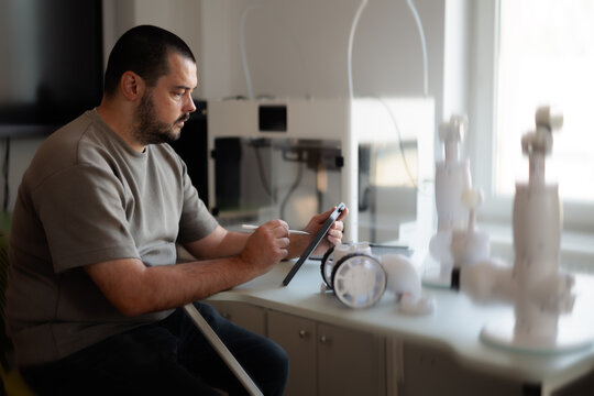Male IT Specialist Programming Advanced Robotics Technology Using Digital Tablet. Engineering professional uses a stylus pen configuring white robotic prototypes in lab