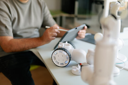 Male Informatics Teacher Programming Robotics Components Using Stylus On Tablet. Engineering professor configures a white electronic robot prototype with his modern device
