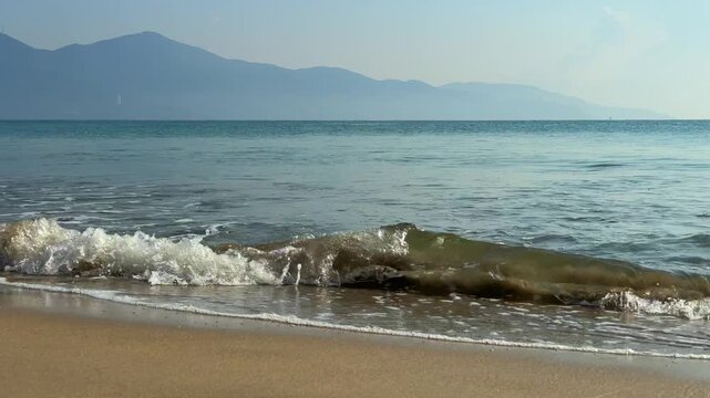 Slow Motion 120fps Waves Breaking on Sandy Beach with Mountains Behind