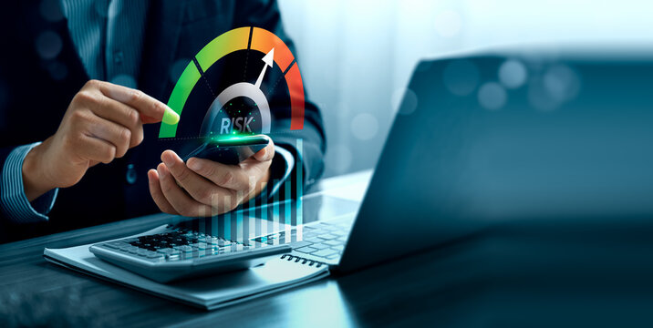 Financial risk assessment concept with business professional using smartphone beside laptop showing virtual risk gauge, rising chart, calculator and corporate decision analysis