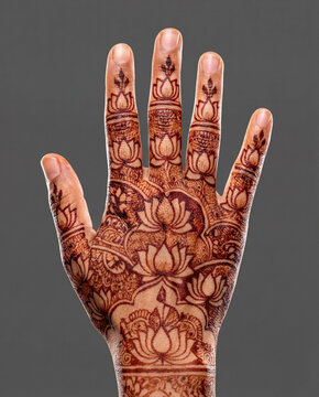 Back of hand adorned with detailed lotus flower henna motifs against a dark gray background