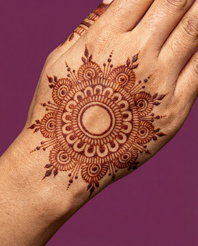 Back of hand decorated with a circular mandala henna design over magenta background