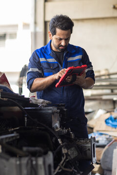 man mechanic using digital tablet while inspecting car engine in garage workshop. Mechanic, automotive, repair, maintenance, technology. Automotive repair concept.