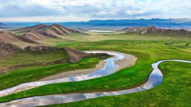 Aerial view of a meandering river flowing through lush green meadows in Bayinbuluke Grassland, Xinjiang, China