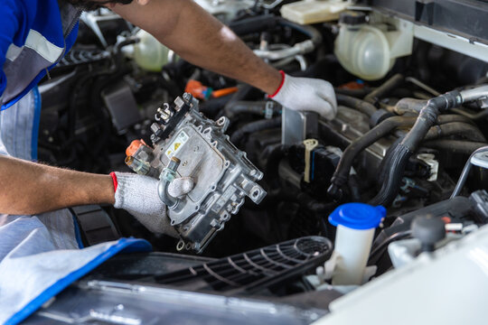 Electric vehicle car technician servicing high-voltage power electronics component inside EV motor bay, automotive maintenance, electrical repair, engineering and electric mobility technology.