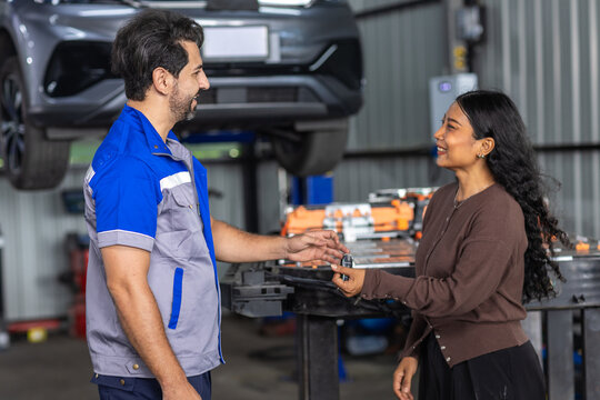 Automotive technician handing car key to female customer in EV service workshop, representing electric vehicle repair, customer service, vehicle handover and professional automotive care.