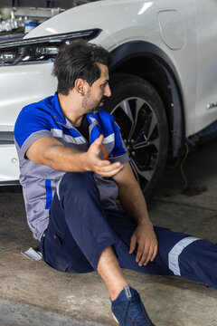Automotive mechanic sitting on the workshop floor beside vehicle after workplace incident, representing occupational safety, accident prevention, injury risk and automotive service hazards.