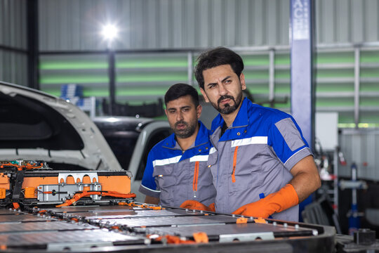 man electric vehicle technicians working on high-voltage EV battery pack in automotive workshop, representing battery maintenance, skilled teamwork, repair and electric mobility technology.