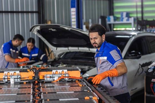 Male automotive technician inspecting electric vehicle battery pack during EV maintenance and diagnostics in auto repair workshop focused on clean transportation technology.