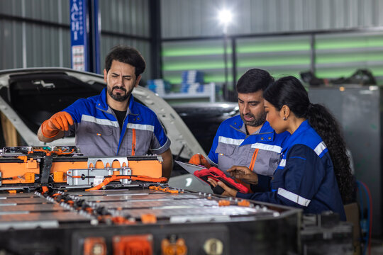 Automotive technician team inspecting electric vehicle battery pack with digital tools during EV diagnostics, maintenance, collaborative service work in repair workshop.