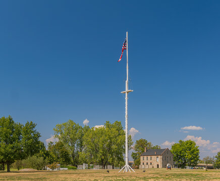 Tall white flagpole with American flag flying above historic stone building