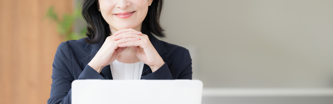 ノートパソコンで仕事をする女性会社員、オフィスで笑顔で働く顎に手を当てるビジネスウーマンのデスクワーク顔無しのバナー