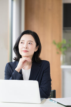 ノートパソコンの前で考える女性会社員、オフィスで仕事やアイデアや企画を悩む、検討する日本人ビジネスウーマン