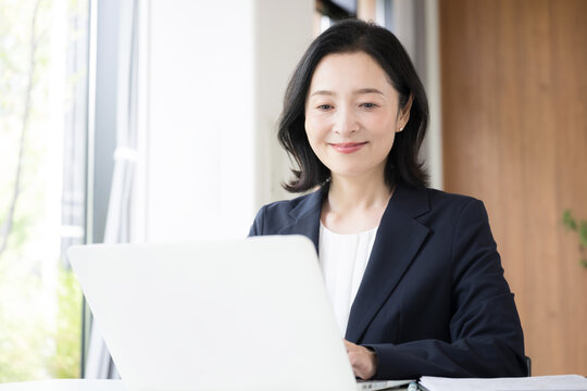 A female office worker working on a laptop; a businesswoman working with a smile at her desk in the office