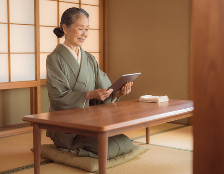 Senior japanese woman in kimono sitting in traditional tatami room using digital tablet for telehealth