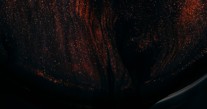 Ink spill. Sparkling fluid. Defocused orange golden color glitter mix acrylic texture floating on abstract art dark background.