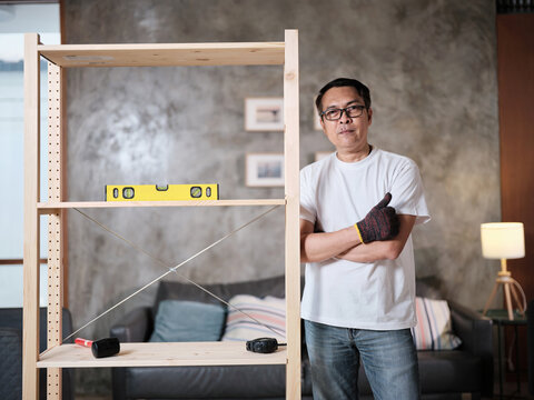 Asian mature man assembling furniture with DIY tools, checking accuracy with spirit&nbsp;level, achievement satisfied, cheerful and proud home improvement, hobby wooden workshop handyman, active lifestyle.