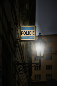 A sign at a police station with the Czech inscription Pomahat a Chranit, Help and Protect, and a bright streetlight in Prague's Old Town