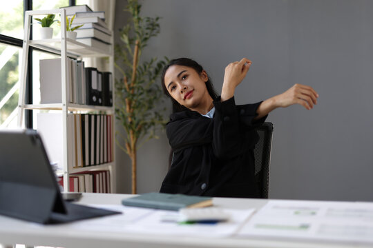 Businesswoman stretching arms at workplace after work on laptop computer.