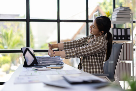 Businesswoman stretching arms at workplace after work on laptop computer.