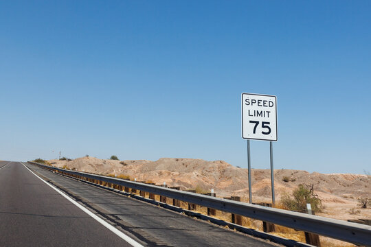 White speed limit seventy five traffic sign stands next to an asphalt highway running through a dry desert landscape under blue sky, Interstate-8 near Wellton, Arizona