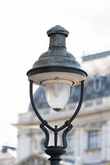 Lamp stands prominently. Facade forms background. Windows frame architecture. Foliage softens surroundings. © VladyslavShcherbakov