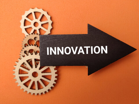 A black wooden arrow reading INNOVATION points to the right over stacked wooden gear wheels on an orange background