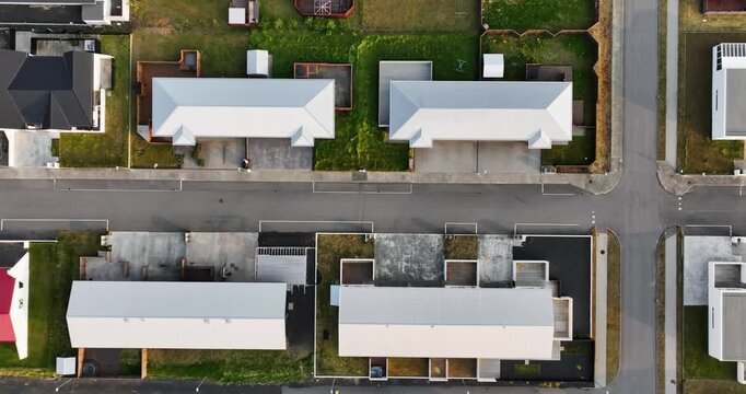 Top-down drone pass over a Grindavik residential block in Iceland, ending beside a visible ground fissure cutting through rocky terrain and pavement near modern homes.